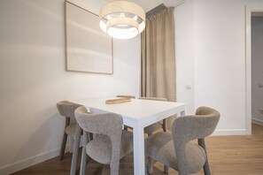 Ein Essbereich mit einem weißen Tisch, sechs grauen Stühlen, einer hängenden Leuchte und einem gerahmten Kunstwerk an der Wand.