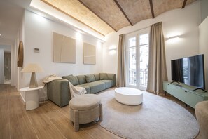Ein modernes Wohnzimmer mit einer Couch, einem Hocker und einem Flachbildfernseher.