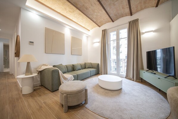 Un salon moderne avec un canapé, un pouf et un téléviseur à écran plat.