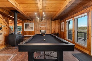 A pool table in a wooden room with a fireplace, framed pictures, and large windows. - The Grand Après | Hot Tub | Gym+Sauna & Theater (Park City)