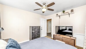 A bedroom with a bed, a ceiling fan, a TV, a dresser, and a door leading to another room. - The Cher e (Cincinnati)