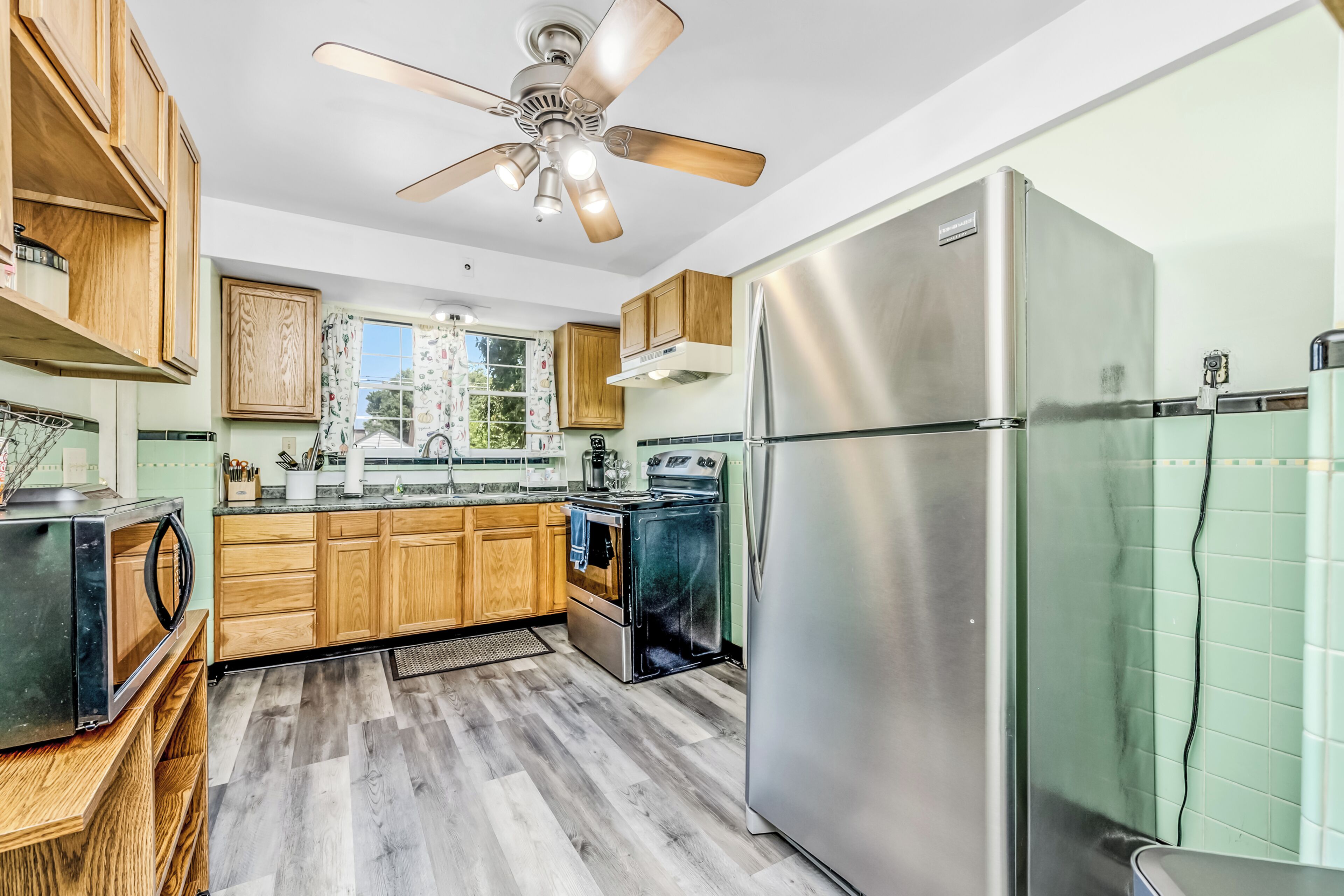 A modern kitchen with wooden cabinets, a stainless steel refrigerator, and a ceiling fan.