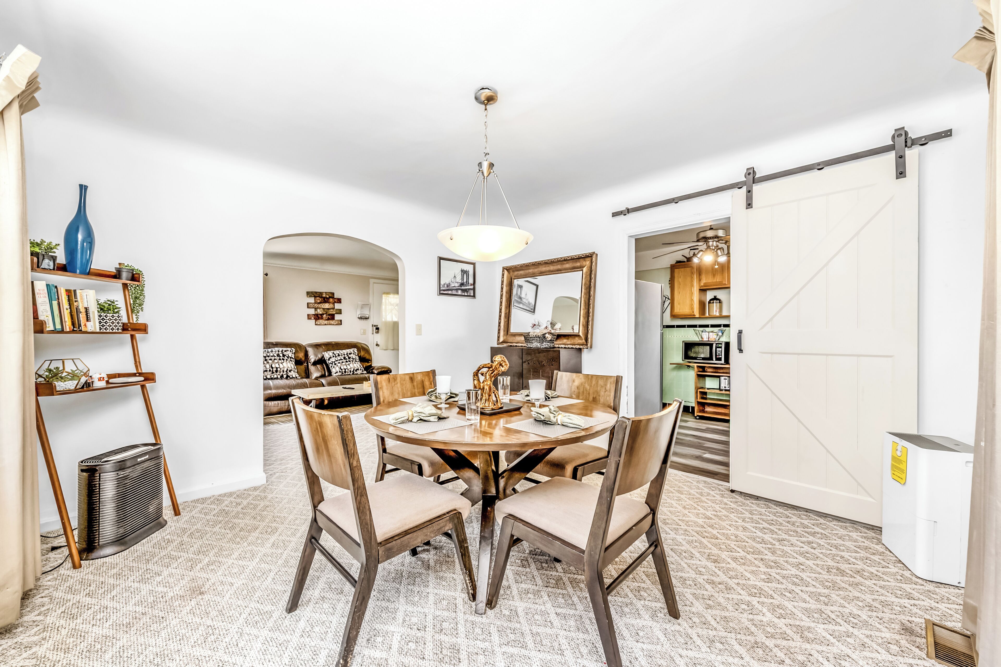 Un comedor con una mesa redonda, sillas y una araña. Se ve una cocina a través de una puerta abierta.