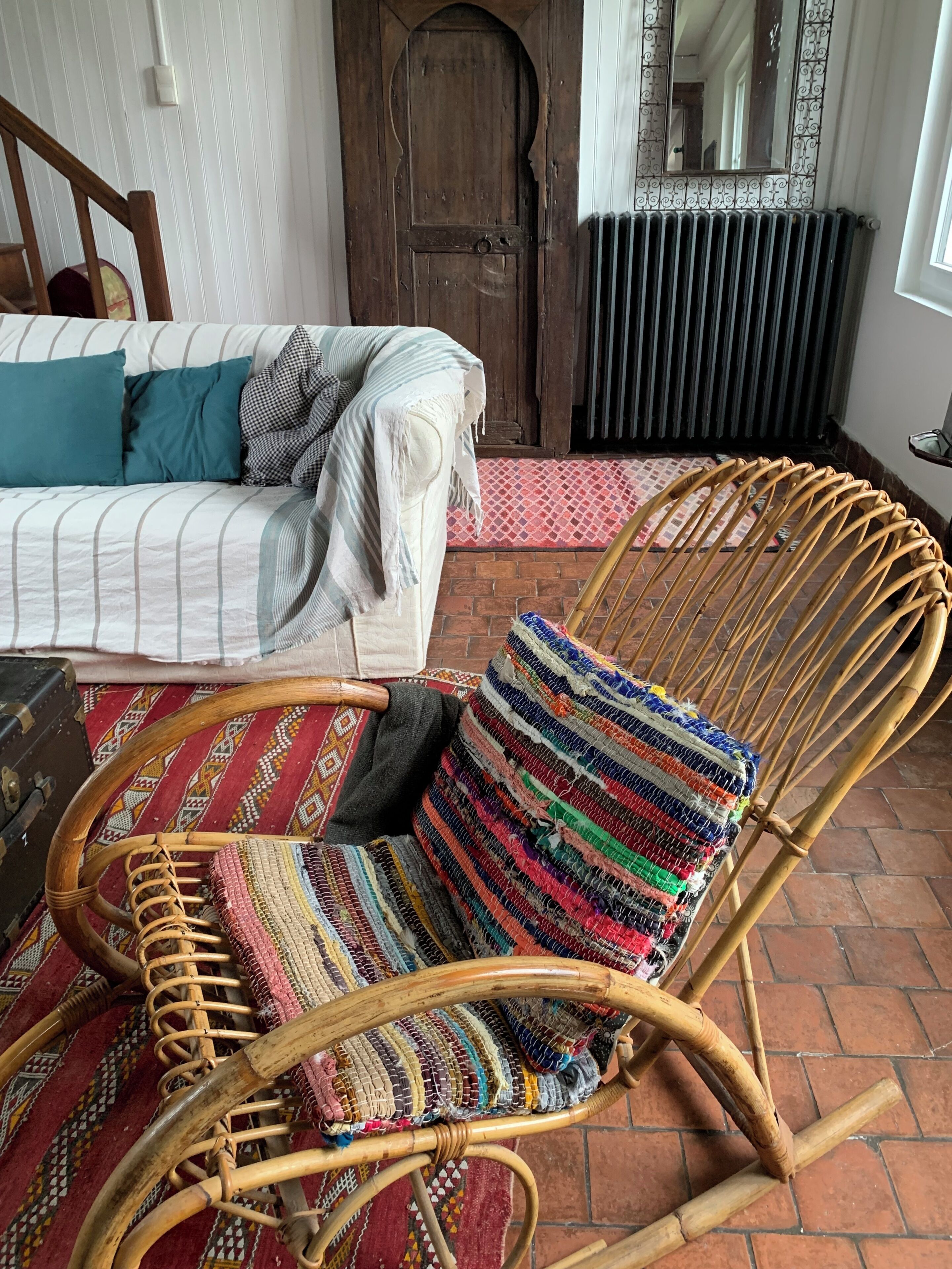 Une chaise en osier avec un coussin coloré à motifs tissés, un canapé à rayures, une porte en bois et un radiateur.