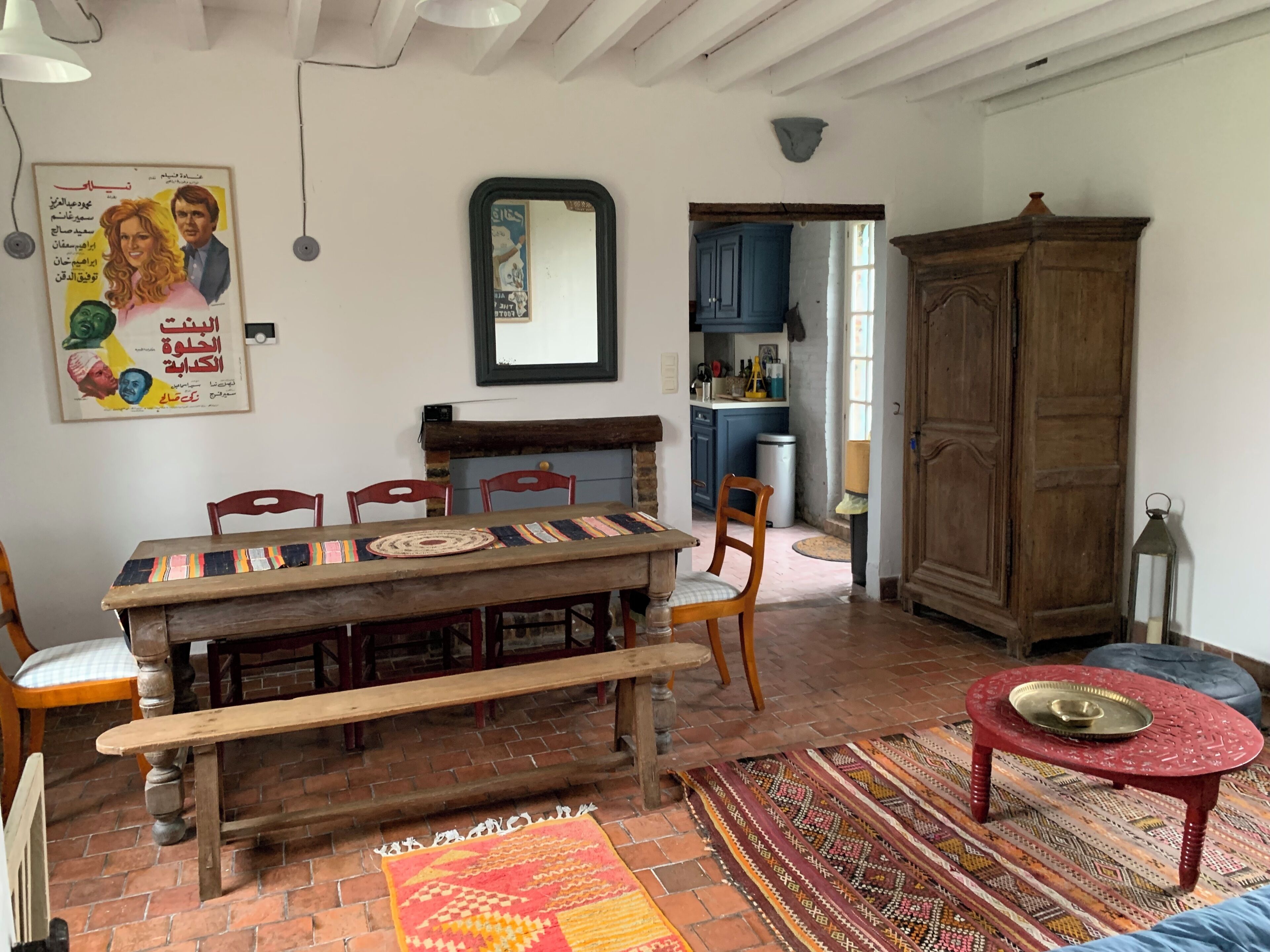 Un coin repas comprenant une table en bois, des chaises, un banc, un tapis, un meuble et un miroir.