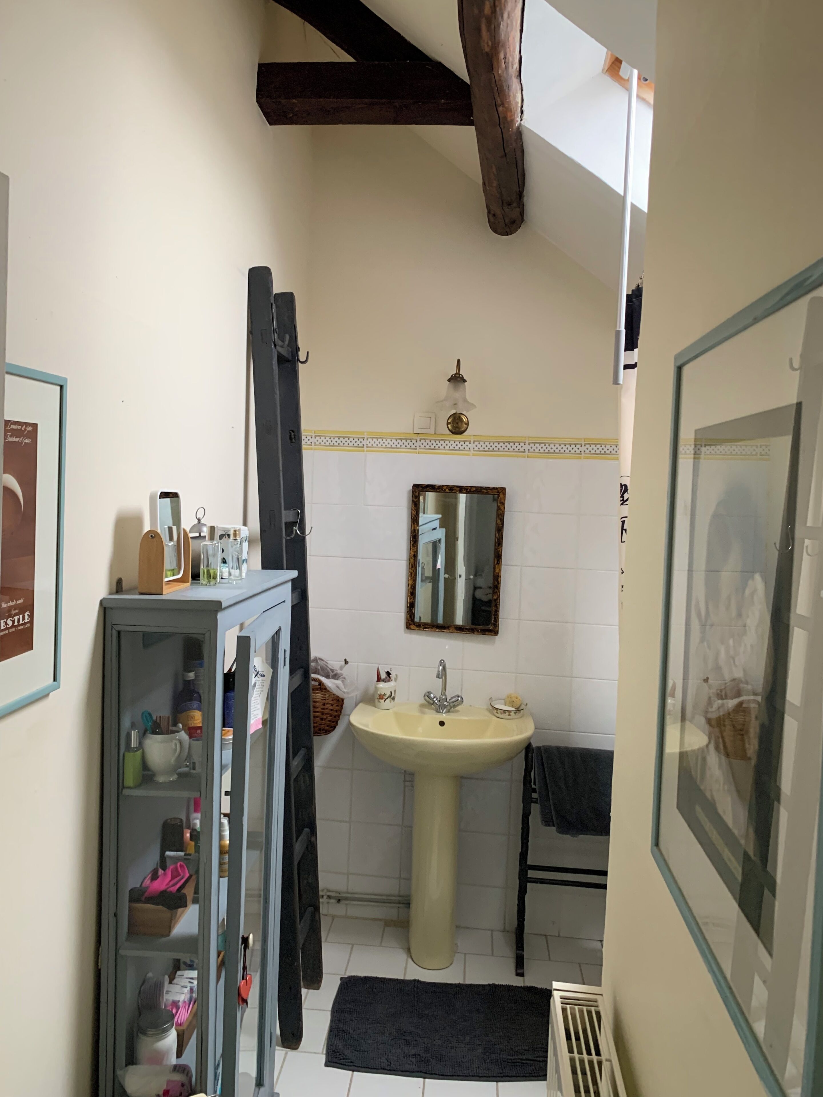 A compact bathroom with a pedestal sink, a mirror, a framed picture, and a cabinet with toiletries.