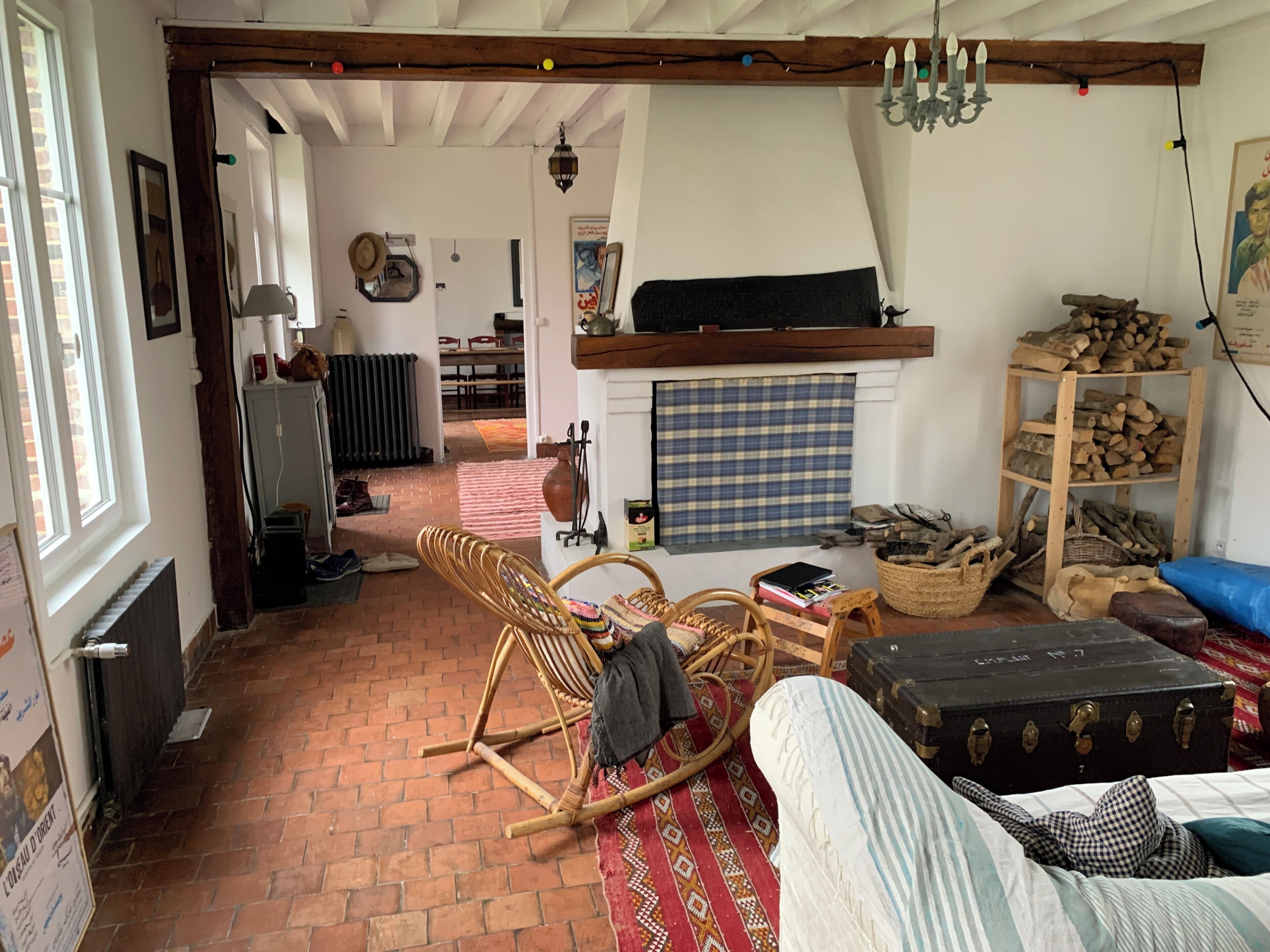 A rustic room with a brick floor, a rocking chair, a sofa, a fireplace, and a wooden shelf with logs.