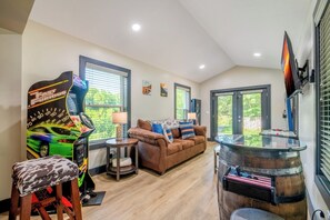 A living room with a gaming console, a couch, a coffee table, and a bar area. - 🦌 Wildlife Cove, Wooded Family Cabin with Arcade Game Room, Sleeps 12 (Sevierville)