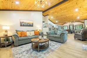 A spacious living area with two sofas, a coffee table, and a dining table. - 🦌 Wildlife Cove, Wooded Family Cabin with Arcade Game Room, Sleeps 12 (Sevierville)