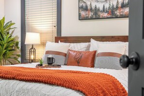 A neatly made bed with a white and orange blanket, a wooden headboard, and a painting of a forest on the wall. - 🦌 Wildlife Cove, Wooded Family Cabin with Arcade Game Room, Sleeps 12 (Sevierville)