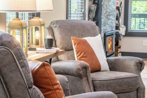 A cozy living room with a fireplace, leather armchairs, and a table with a book and a mug. - 🦌 Wildlife Cove, Wooded Family Cabin with Arcade Game Room, Sleeps 12 (Sevierville)