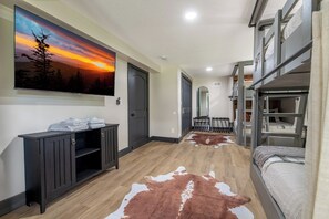 A bedroom with bunk beds, a mounted TV, a cowhide rug, and a cabinet with towels. - 🦌 Wildlife Cove, Wooded Family Cabin with Arcade Game Room, Sleeps 12 (Sevierville)