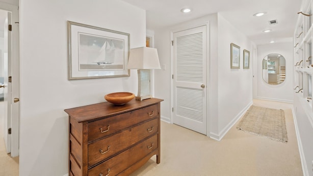 A hallway with a wooden dresser, a framed picture, a lamp, and a door with louvered shutters. - Steps from the ocean in Debordieu (Georgetown)