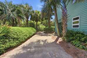 A paved pathway leading to a house with a green exterior, surrounded by lush greenery and palm trees. - Steps from the ocean in Debordieu (Georgetown)