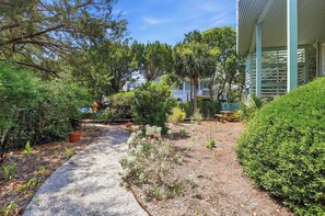 A pathway leading to a building with a covered porch area, surrounded by various types of vegetation and a small garden. - Steps from the ocean in Debordieu (Georgetown)