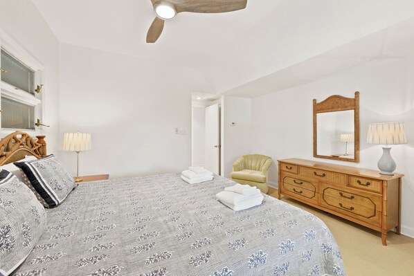 A bedroom with a bed, a wooden dresser, a chair, a ceiling fan, and a mirror.