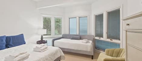 A bedroom with a bed, a sofa, a chair, a ceiling fan, and a window with blinds.