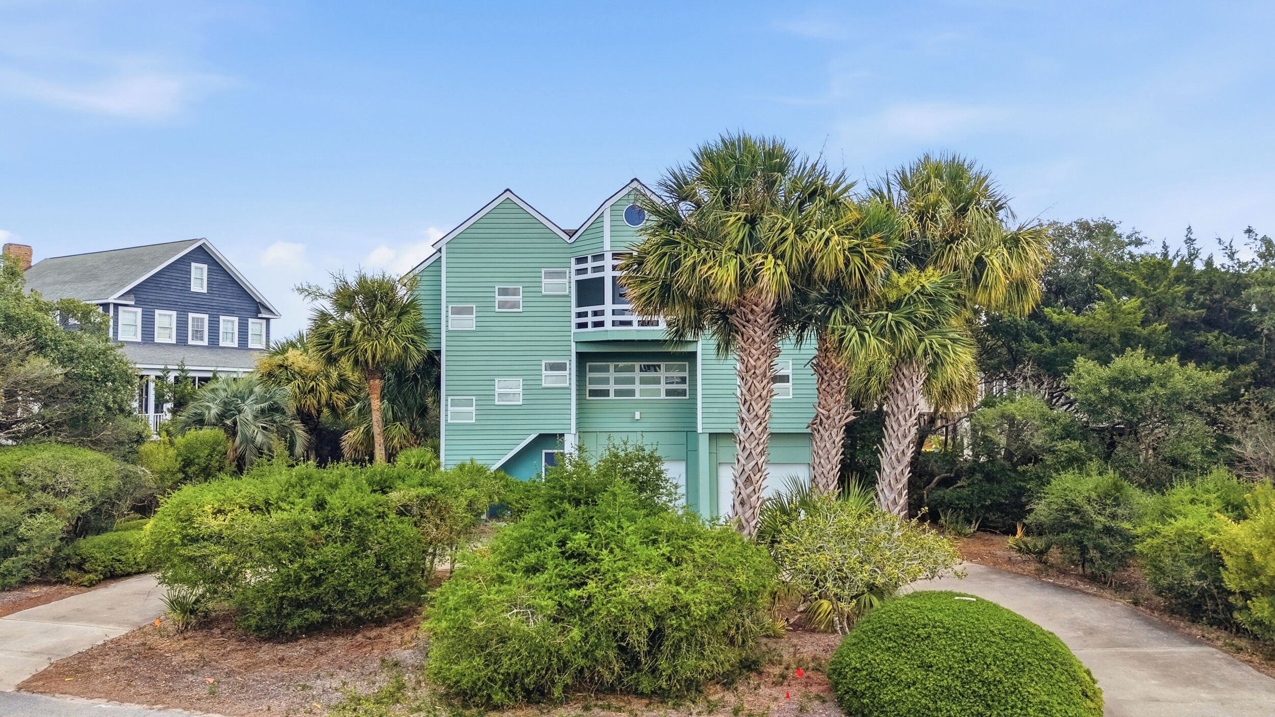 A two-story house with a green exterior, surrounded by lush greenery and palm trees.
