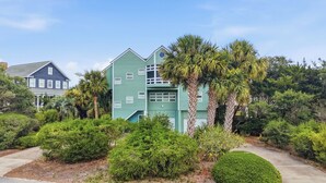 A two-story house with a green exterior, surrounded by lush greenery and palm trees. - Steps from the ocean in Debordieu (Georgetown)