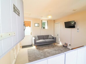 A room with a grey sofa, a television mounted on the wall, a door with a sign, and a window with curtains. - Coach House (Beaworthy)