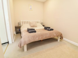 Un dormitorio con cama, almohadas, una mesita de noche con lámpara y un cuadro pequeño en la pared.