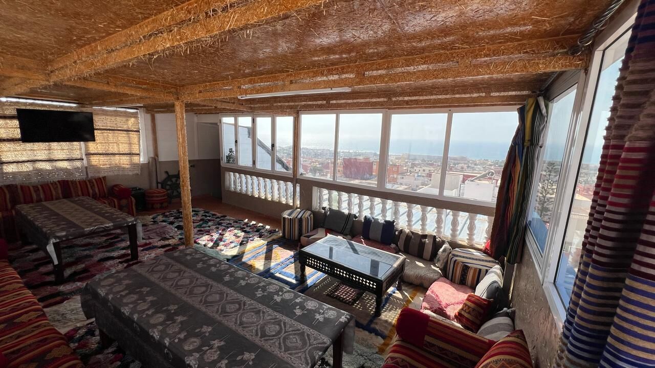 Una habitación con techo alto, ventanas amplias, un conjunto de sofás, una mesa de centro y un televisor.