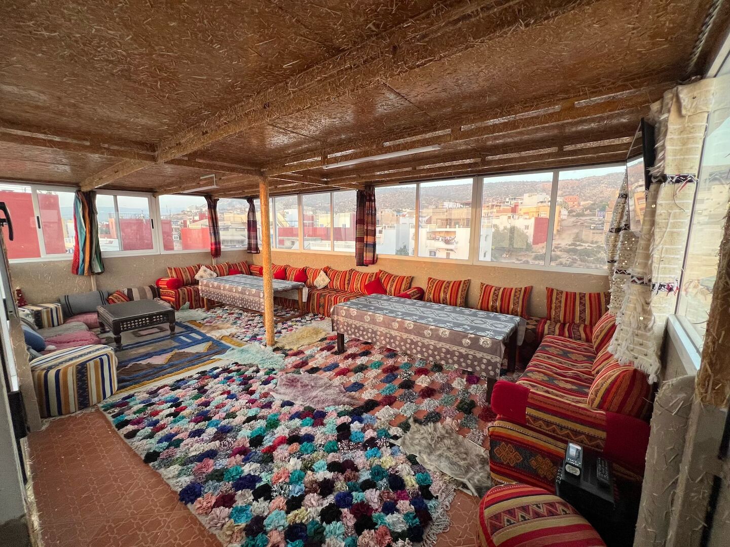 Una habitación con techo alto, ventanas amplias, un conjunto de sofás, un tapete estampado y una pequeña mesa.