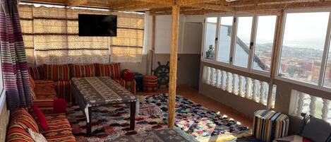 A room with a large window, a television, a table, and a sofa.