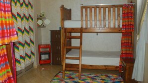 Ein Stockbett mit Holzrahmen, ein kleiner Nachttisch, ein roter Heizkörper und ein farbenfroher Teppich.