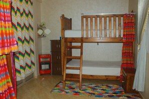 Una cama nido con estructura de madera, una mesita de noche pequeña, un calentador rojo y una alfombra colorida.
