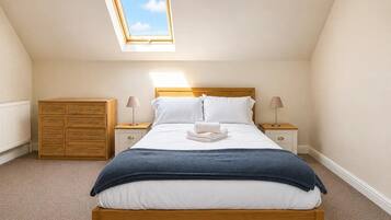 A bedroom with a skylight, a bed with white linens, a wooden dresser, and two bedside tables with lamps.