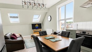 Una cocina moderna con horno empotrado, un comedor con mesa y sillas de madera, un sofá y un televisor sobre un mueble.