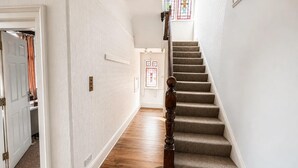 Un pasillo con una escalera alfombrada, paredes blancas y una puerta que da a una habitación con ventana.