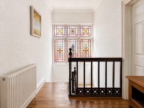 A hallway with a wooden floor, a white radiator, a black railing, and a stained glass window with floral patterns.