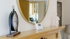 Ein hölzerner Konsolentisch mit einem runden Spiegel, einer Wanduhr, einem Thermostat und einer weißen Skulptur.