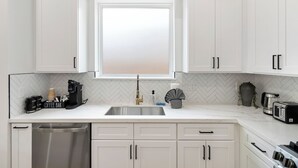 Una cucina moderna con mobili bianchi, un lavello in acciaio inossidabile, un angolo caffè e un tostapane.