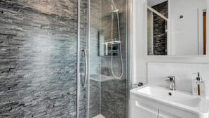 Ein modernes Badezimmer mit einer gläsernen Dusche, einem weißen Waschbecken und einem Spiegel darüber.