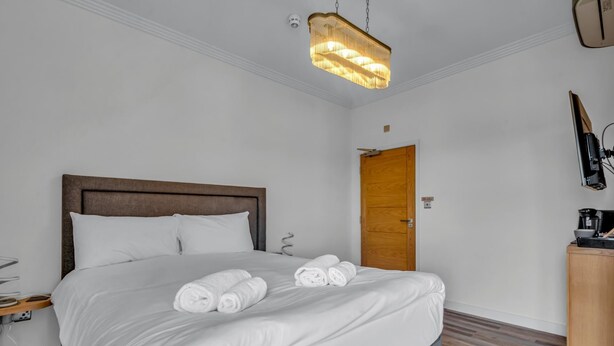 Ein Hotelzimmer mit einem Bett, einem hölzernen Kopfteil, einem Schrank aus Holz, einem Schreibtisch mit Stuhl und einer Pendelleuchte.
