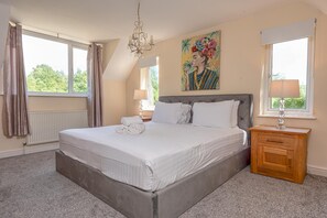 A bedroom with a large bed, a chandelier, a painting, and a view of trees.