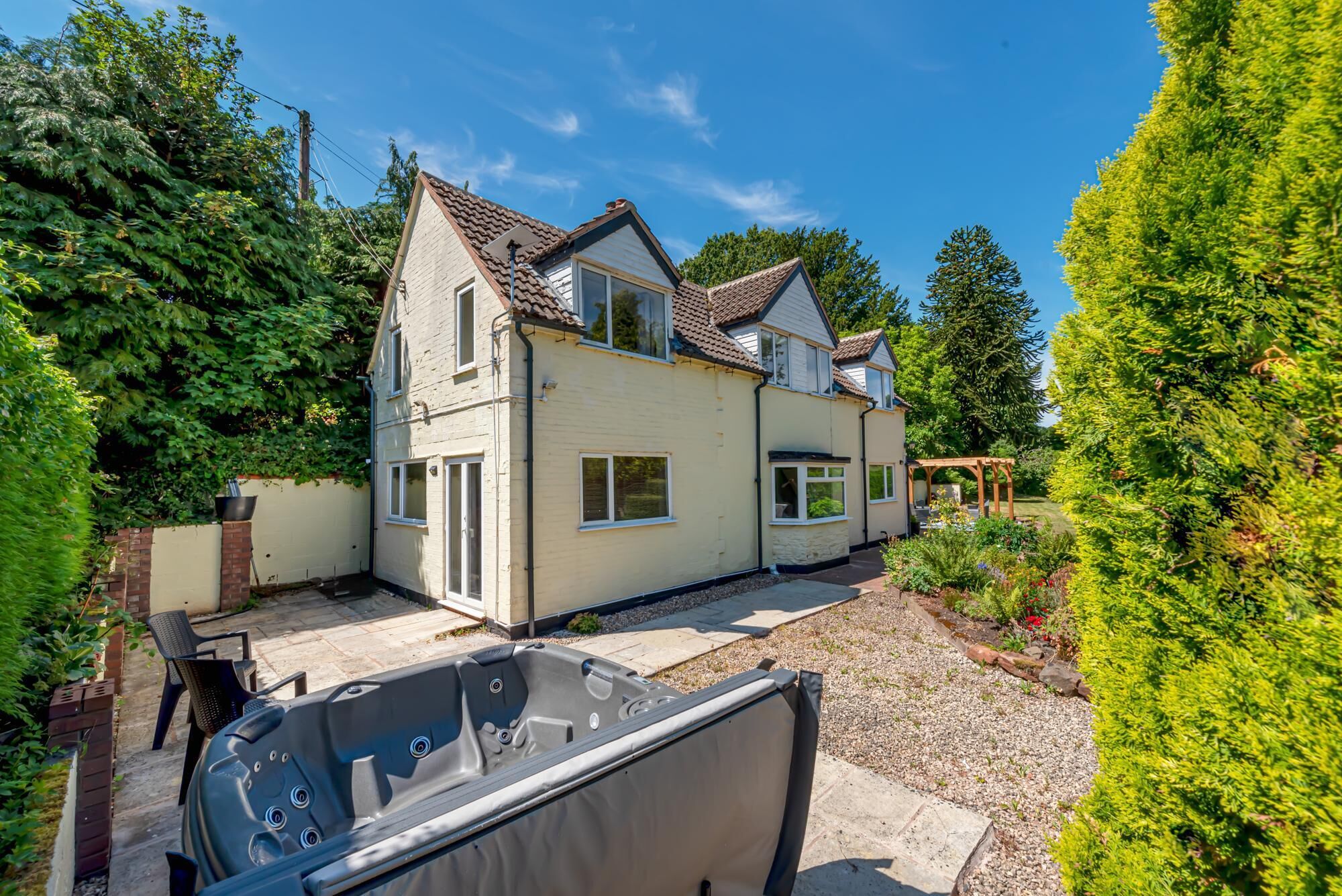 Een tweelaags huis met een patio, een jacuzzi en een tuin met diverse planten en een houten pergola.