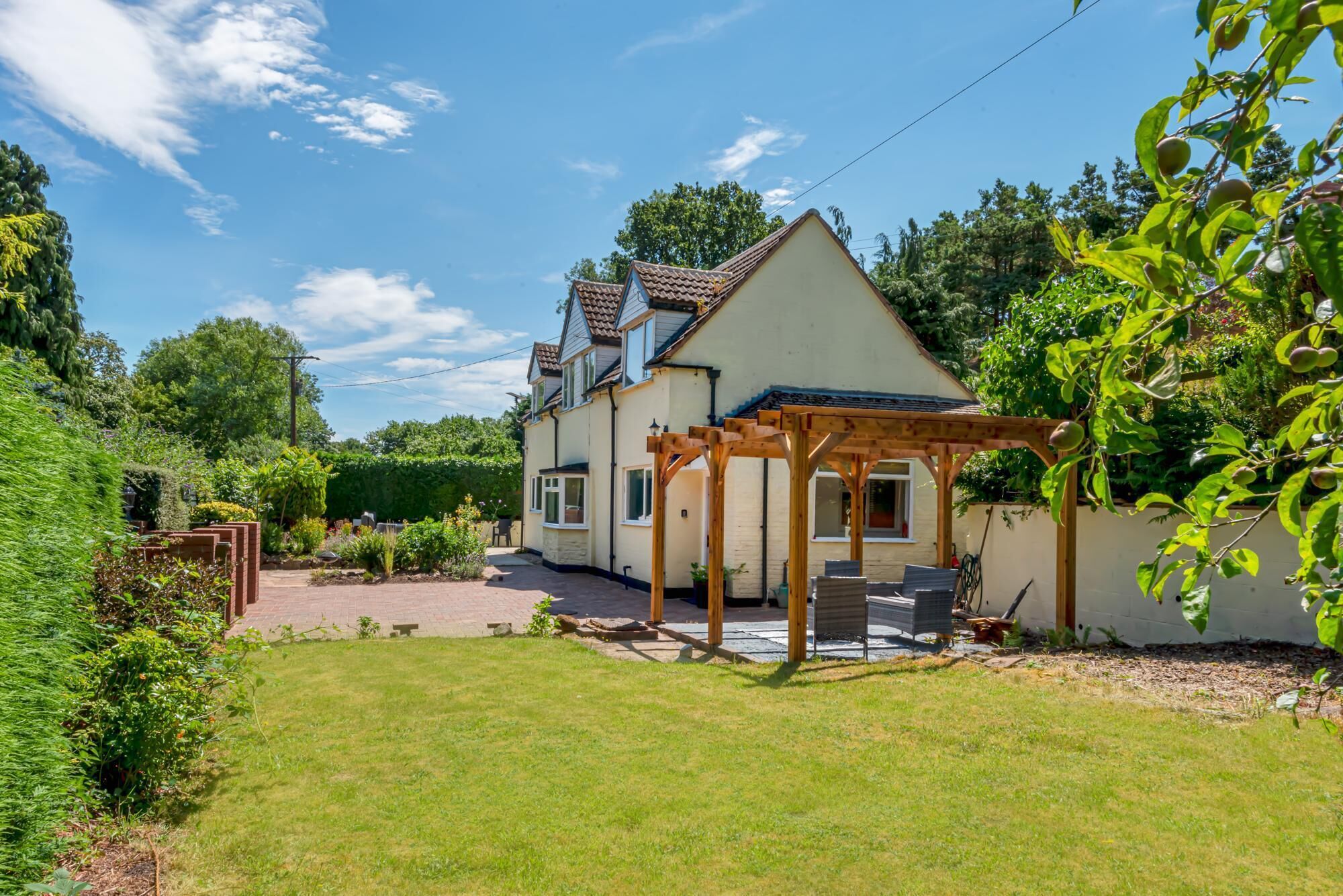 A two-story house with a covered patio area, surrounded by a well-maintained garden and trees.