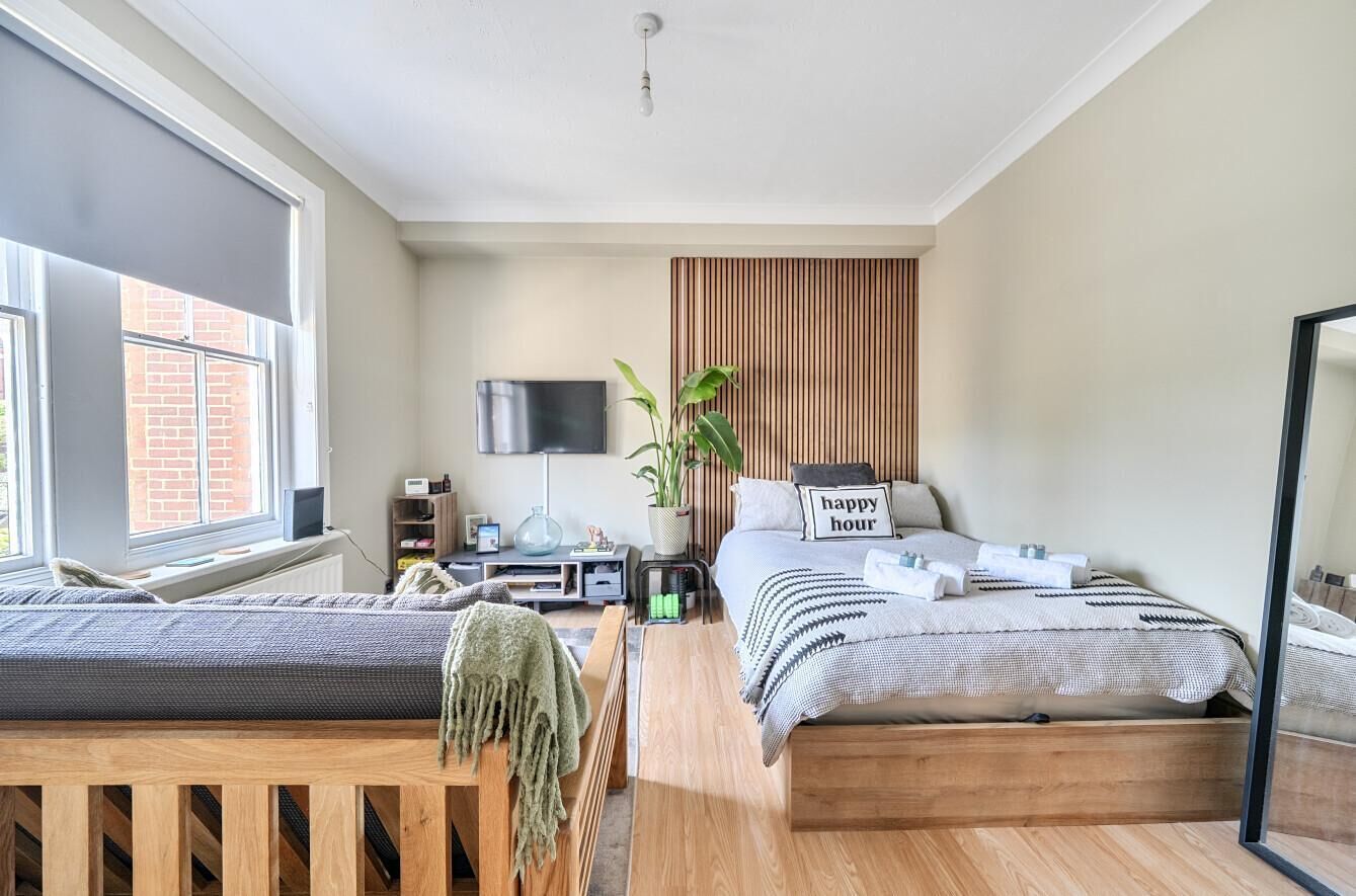 A modern bedroom with a bed, bedside table, TV, and a window.