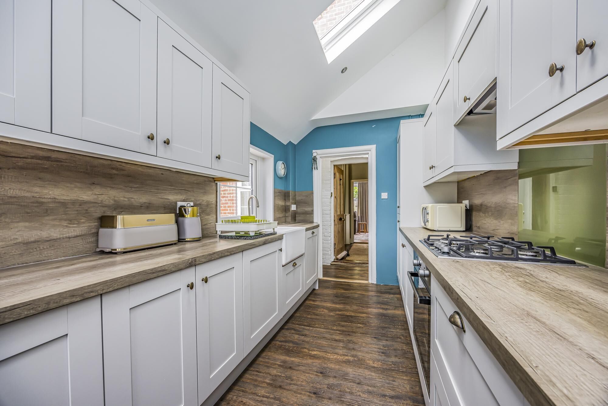 A narrow kitchen with white cabinets, a wooden countertop, and a gas stove.