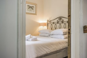 A neatly made bed with white linens, a metal headboard, and a framed botanical print on the wall. - Number 2 Admiralty Cottages - Pass the Keys (Gosport)