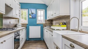 Eine schmale Küche mit weißen Schränken, einer blauen Wand, einem Fenster und einer Heizung.