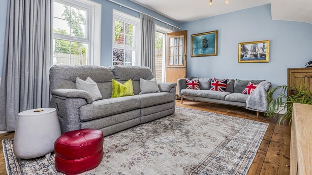 Ein Wohnzimmer mit grauem Sofa, Fußhocker in Rot und einem gemusterten Teppich.