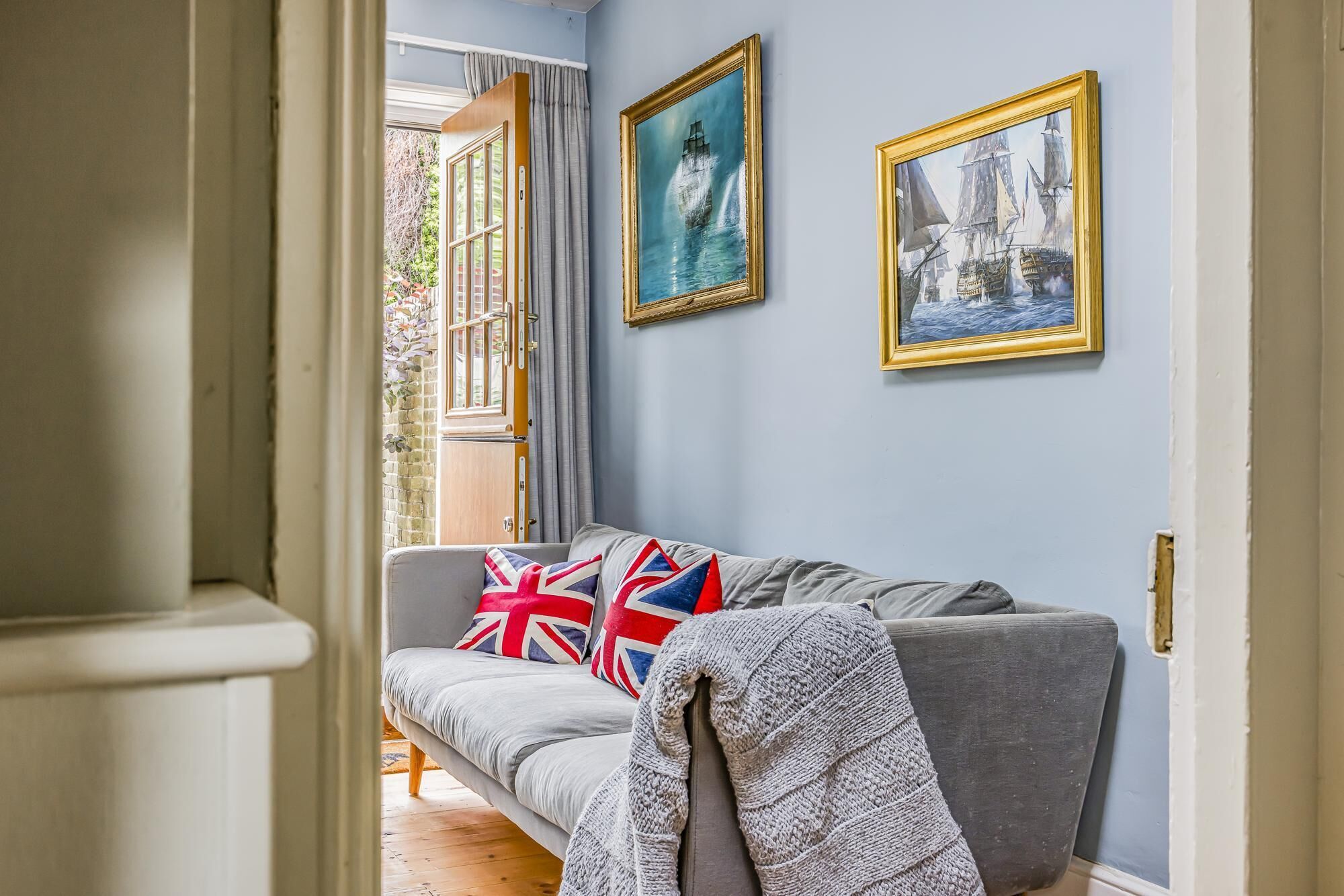 A hallway with a grey sofa, two framed paintings, and a window with curtains.