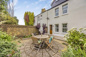 A patio with a round table and chairs, surrounded by plants and a brick wall. - Number 2 Admiralty Cottages - Pass the Keys (Gosport)