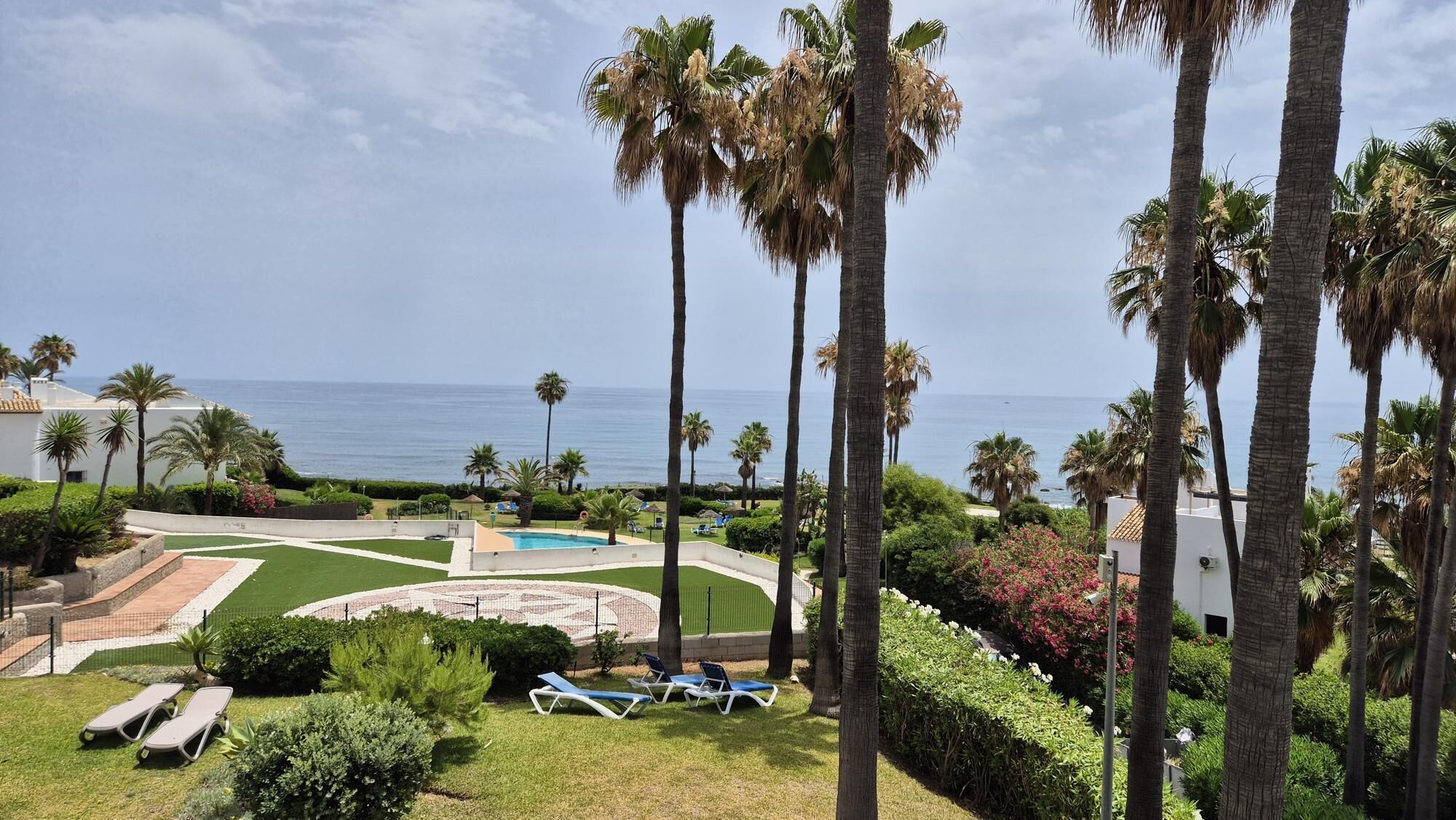 Ein Poolbereich mit Liegestühlen, Palmen und Blick auf das Meer.