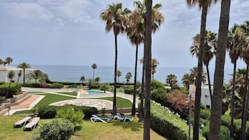 Ein Poolbereich mit Liegestühlen, Palmen und Blick auf das Meer.